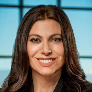 C. Brett Marottoli is a woman with long straight brown hair. She has on makeup and a smile, and is posing for a professional headshot. The background of the image is a light blue.