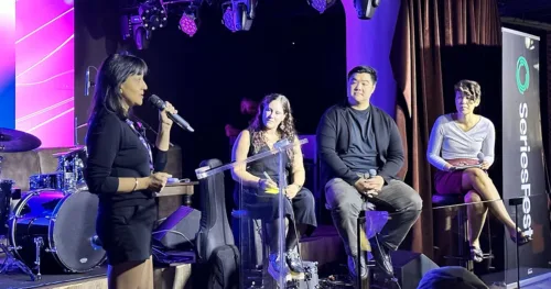 Woman speaks into microphone on stage with 3 others listening intently